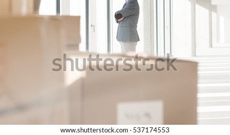 Distant image of businessman looking through window with cardboard boxes in foreground