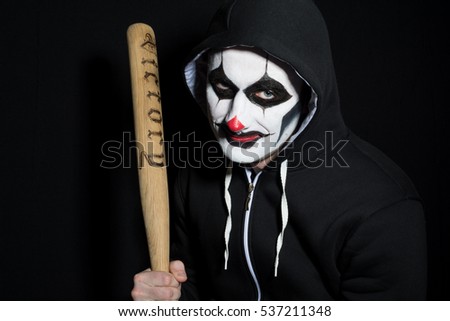the portrait of a men in a make-up of the clown with a bat in hands against a dark background