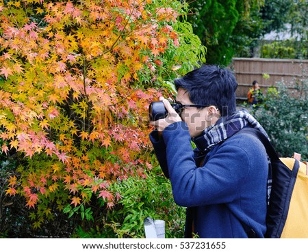 Asian man taking photo with autumn leaves background