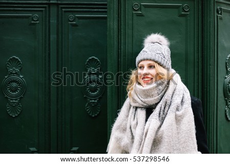 Pretty young blonde girl posing near green antique metal work wall in winter clothes smiling and looking in the distance, with red lips having fun alone - subject on the right side of the photo