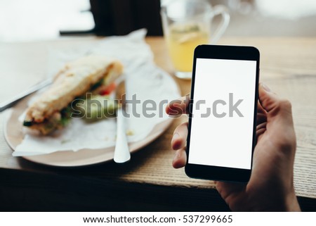 Young man's hand holding mobile phone. He is sitting in restaurant or cafe. He is trying to watch a video or movie. Place for your advertisment or logo. Close-up. Horizontal position of the phone