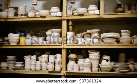 many different pottery standing on the shelves in a pottery workshop. Low light