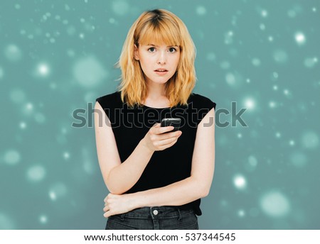 Young beautiful woman using mobile phone studio on gray color background with snow snowflakes winter