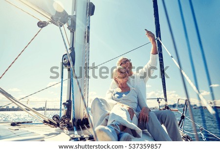 sailing, technology, tourism, travel and people concept - happy senior couple with smartphone taking selfie on sail boat or yacht deck floating in sea