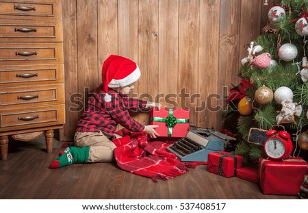 Very happy cute Boy with xmas gifts on wooden background. Child in santa hat. Happy christmas and new year holidays. Space for text. Boy in plaid shirt and suspenders. New Year and Christmas tree