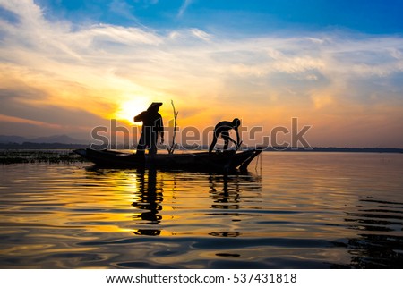 Lifestyle of Asian fisherman on wooden boat   for catching freshwater fish in reservoir in the  early morning before sunrise