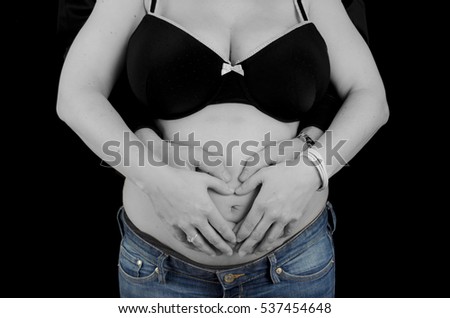 Father and mother to be holding their hands on the pregnant belly in grey scale with blue jeans