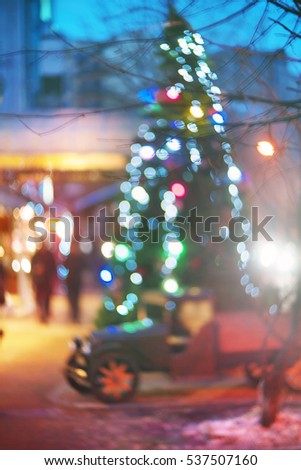Evening city picture with defocused effect blur Lenses gives lightness and fabulousness. Illumination and fabulous silhouette of people going shopping for Christmas