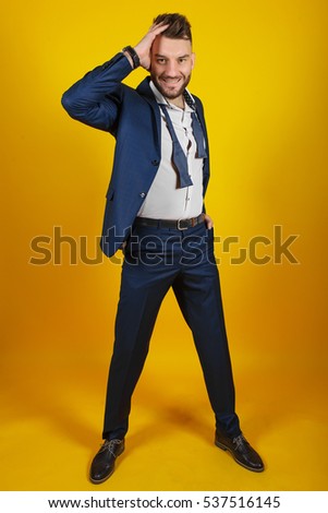 Smiling business man in blue suit pointing at copy space over yellow background