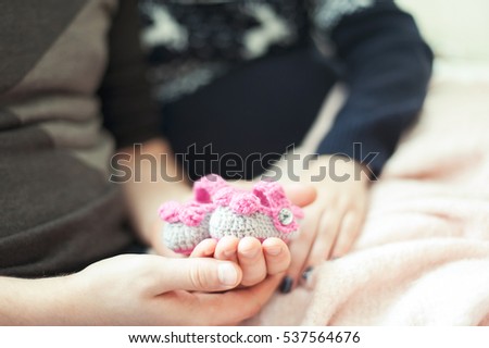 Young happy future parents hands holding woollen knitted newborn baby booties. Indoors horizontal colored close-up image with soft vintage filter.