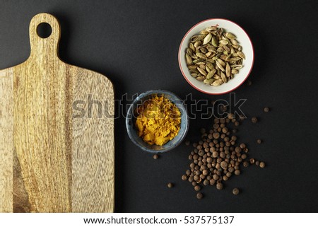 Cutting board with bowls with tumeric, cardamom on black background. Space for text