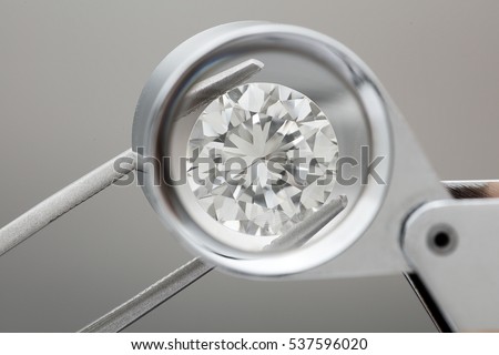 loose brilliant round diamonds is being held by tweezers and looked through a loupe Royalty-Free Stock Photo #537596020