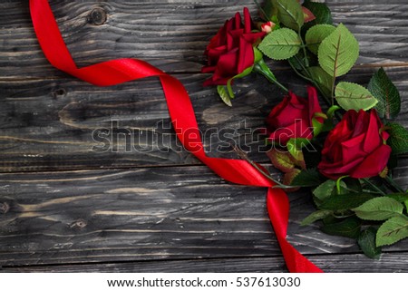 Greeting card with roses and red ribbon on the wooden background