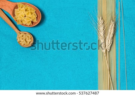 Pasta in wooden spoons,  spaghetti and wheat on a blue background.