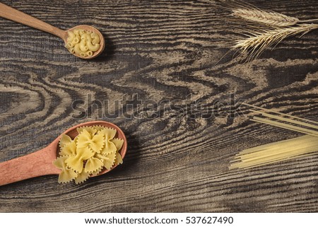 Pasta  in wood spoons,  spaghetti and wheat on a wooden background. Bright and cheerful picture