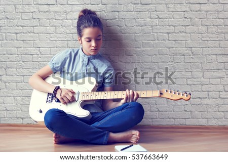 Beautiful young girl plays guitar and composes music on a background of a brick wall. Royalty-Free Stock Photo #537663649