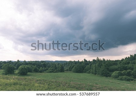 countryside fields in autumn with forests in background and clouds above - vintage effect