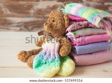 Stack of baby clothes with teddy bear in pastel color range on a wooden background