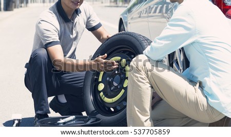 Picture of a male mechanic replacing a car tire with his client on the road