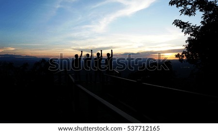 Silhouette of four people standing on the highest point of the mountain, show hands up symbolic meaning successful.
