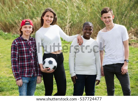 Portrait of four friends posing on countryside field with ball in sunny day