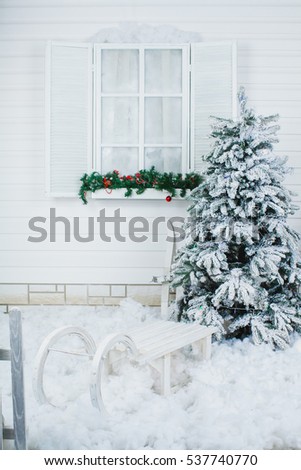an exterior with a fence, a sled and a christmas tree at a a window of a white wooden house
