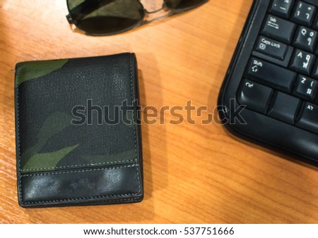Wallet and sunglasses and keyboard on wooden table.