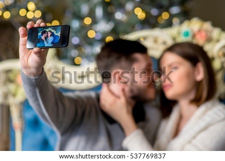 Couple of lovers taking selfie on smartphone lying on the sofa in Christmas time. Christmas interior. Holiday at home