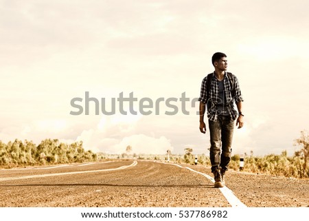 Wanderer or loner walking down an empty road and hot. Road hitch-hiking. Royalty-Free Stock Photo #537786982
