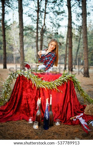 Beautiful girl having tea in the forest. Table with candles and tea in the forest.