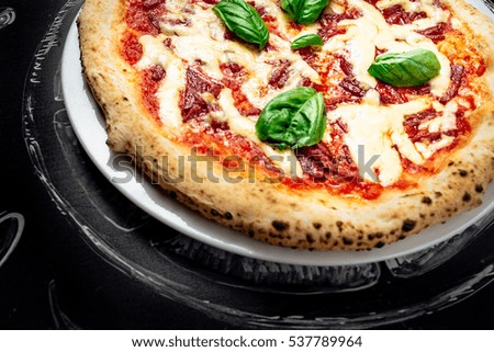 Italian food, menu, restaurant concept, pizza with  cheese, olives, basil, sausage, tomatoes on white plate on black background, space for text