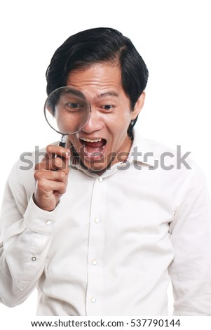 Photo image portrait of a funny young Asian businessman looked very happy, surprised and smiling to find something while looking into magnifying glass, close up portrait over white