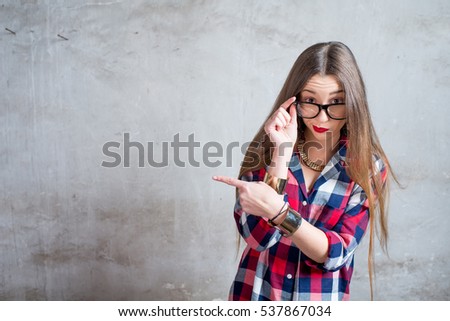 Portrait of watchful woman in the red checkered shirt with eyeglasses on the gray textured wall background
