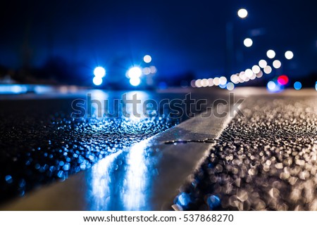 Rainy night in the big city, the car traveling on the highway and shines a blinding light. Close up view from the level of the dividing line, image in the blue tones Royalty-Free Stock Photo #537868270