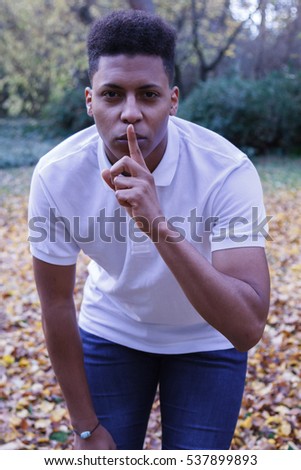 Young black African man sending silence. He puts his finger to his lips as a gesture to silence. 