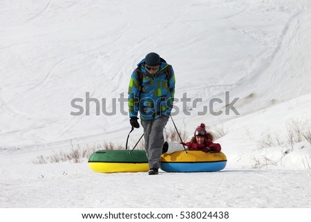 Father and daughter with snow tube in sun winter day. Caucasus Mountains, Georgia, region Gudauri