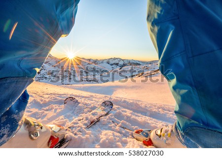 Ski athlete standing in front of wonderful sunset  on top of the mountain - Legs view of young skier with sun back light - Sport and vacation concept - Focus on skis - Warm filter