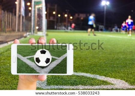 Man use mobile phone, blur image of football field as background.