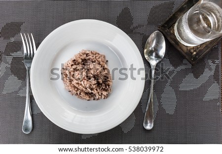 Cooked Brown/Red Rice on dish with spoon, fork and a glass of water