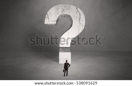 A small elegant business person in suit standing with his back in front of a huge question mark in open space concept