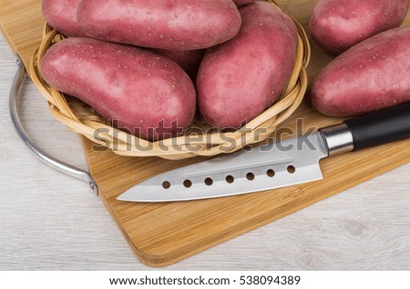 Raw red potato in wicker basket and kitchen knife on bamboo cutting board