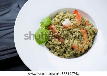 Closeup of a white plate with spinach and tiger shrimps risotto, selective focus