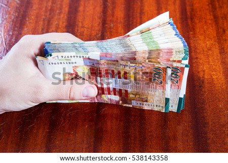 A female hand holding two hundred shekel bank notes against wood background. Concept photo of money, banking ,currency and foreign exchange rates.