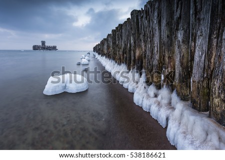 Winter landscape at the sea. Frozen wooden breakwaters line to the world war II torpedo platform (polish name torpedownia ) at Baltic Sea.  Morning at Babie Doly, Poland. Long exposure photo.