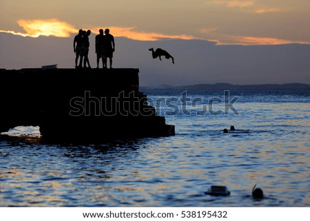 Young Brazilian kids jumping into the sea from the rocks at Porto da Barra beach.