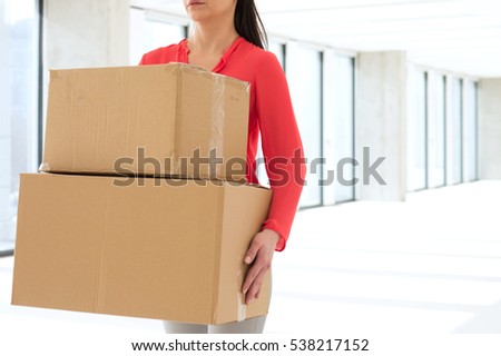 Mid adult businesswoman carrying cardboard boxes in new office