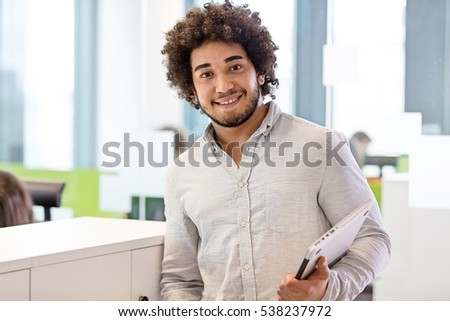 Portrait of smiling young businessman holding laptop in office