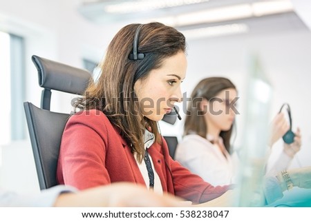 Young businesswoman using headset with female colleague in background at office