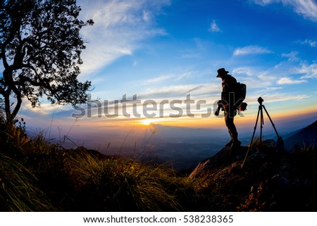 Silhouette of Young man with backpack taking a photo on the top of mountains