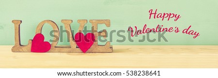 Valentines day background. Word LOVE from wooden letters and red hearts on old table. Filtered and toned image